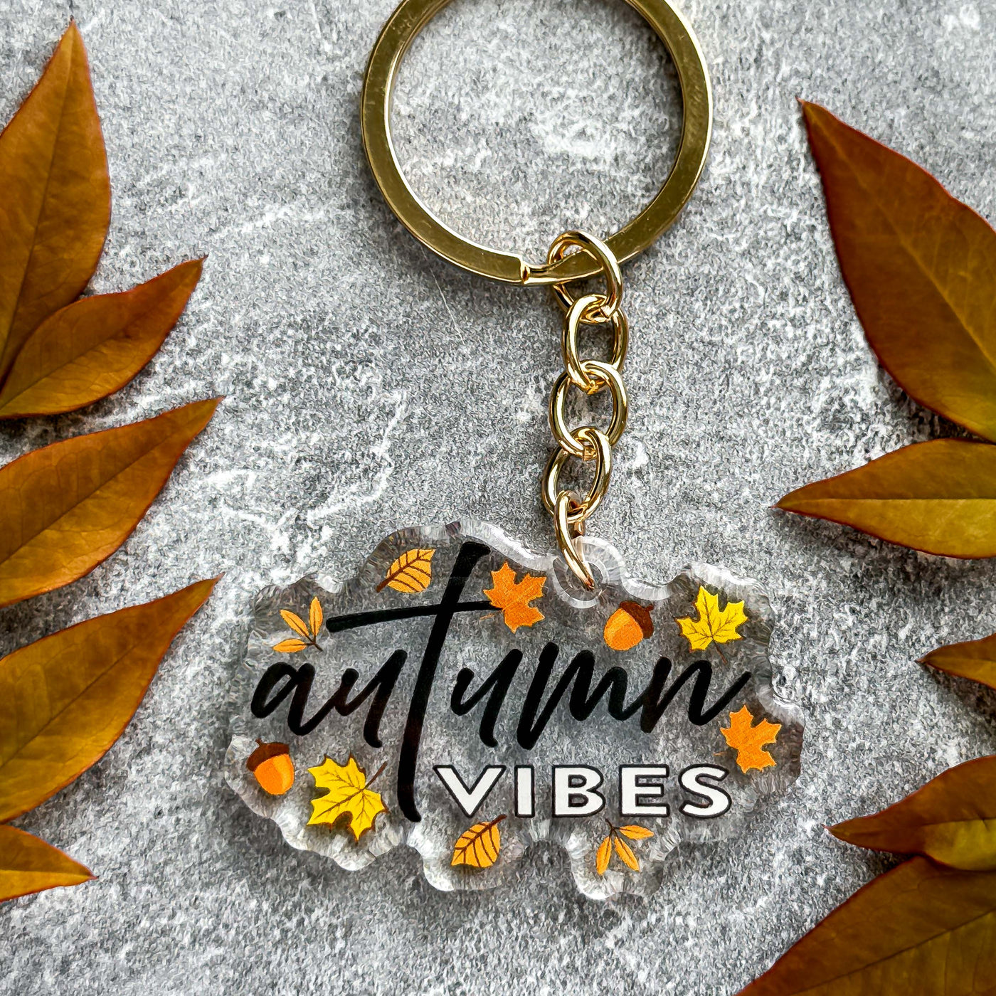 Keychain with 'autumn vibes' text surrounded by autumn leaves on a gray surface.