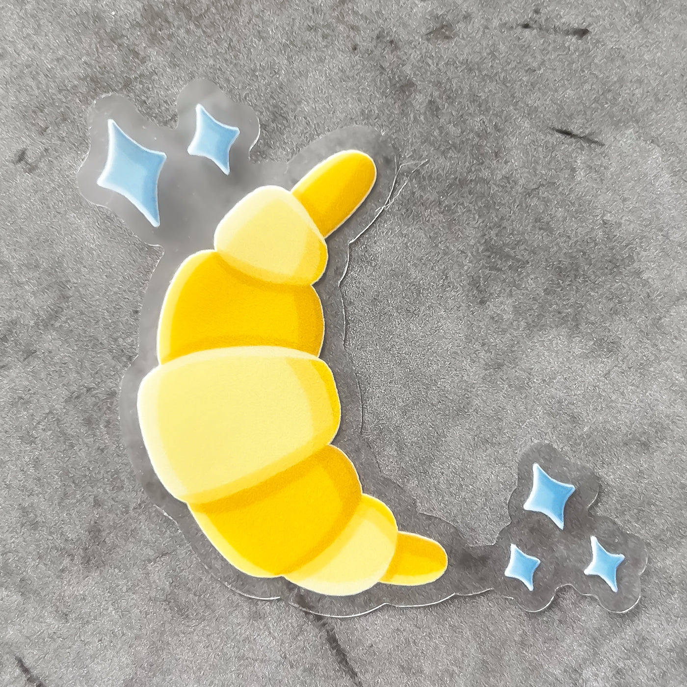 Croissant vinyl sticker, offered in classic white with white background and white border or clear sticker with a solid white backing, but is clear once the backing is removed. Food stickers by Simpliday Paper by Olga Nagorna.
