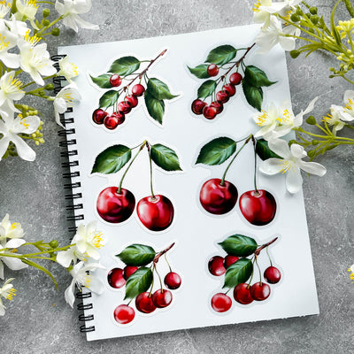 Notebook with cherry illustrations surrounded by flowers on a gray surface