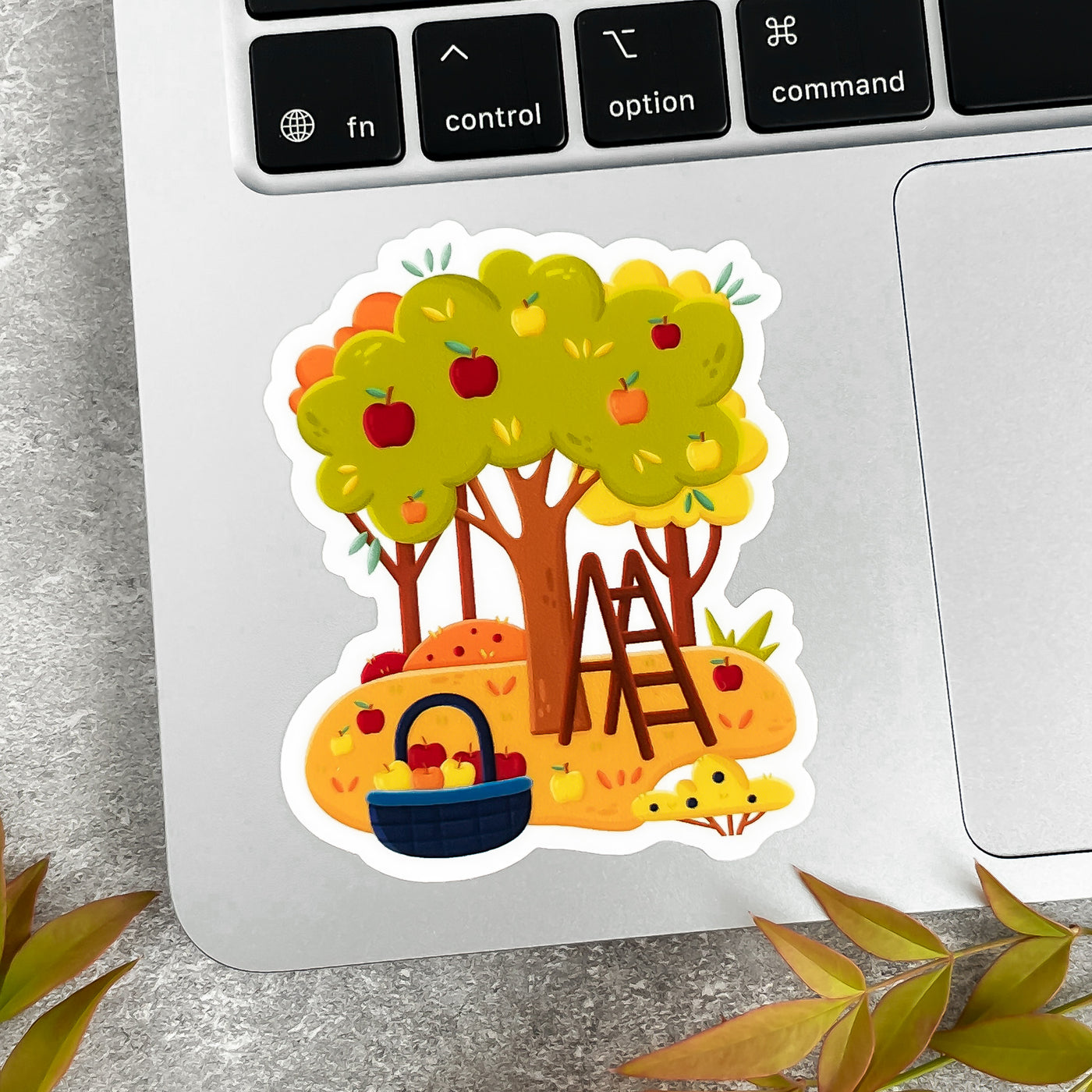 Colorful sticker of a tree with apples, ladder and basket on a laptop keyboard.