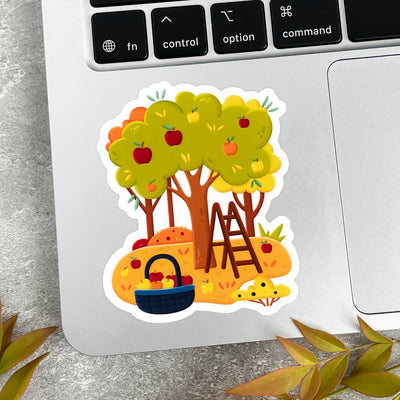Colorful sticker of a tree with apples, ladder and basket on a laptop keyboard.