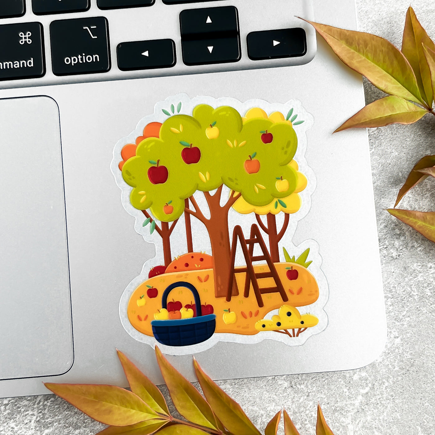 Sticker of a tree with apples, a basket, and a ladder on a laptop keyboard.