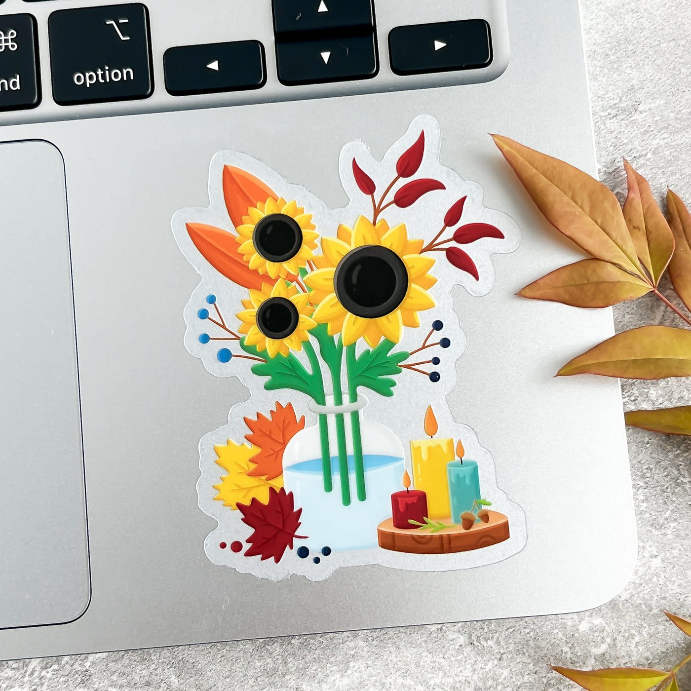 Decorative sticker with sunflowers, candles, and leaves on a laptop keyboard.