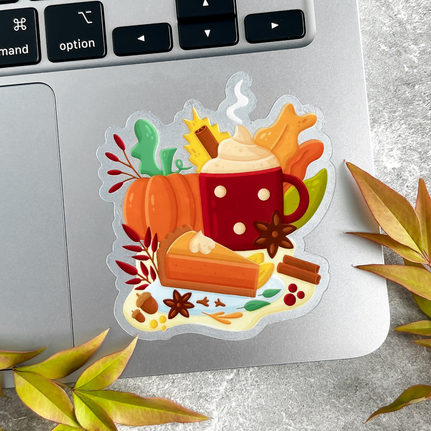 Decorative sticker with a cup of hot chocolate, pumpkin, and autumn leaves on a laptop keyboard.