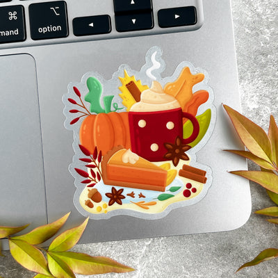 Decorative sticker with a cup of hot chocolate, pumpkin, and autumn leaves on a laptop keyboard.
