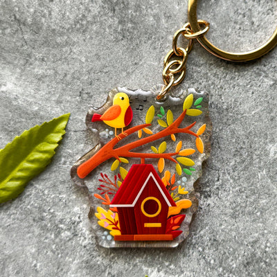 Keychain with birdhouse and bird design on a gray surface.
