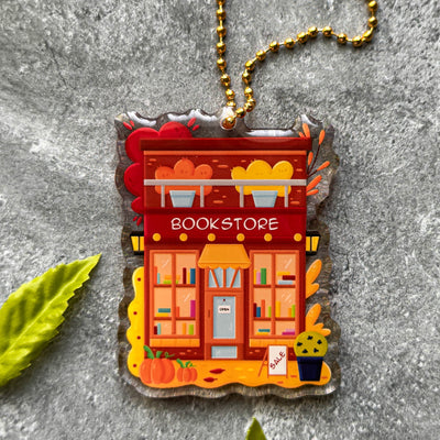 Decorative keychain of a bookstore with a gold chain on a gray surface.