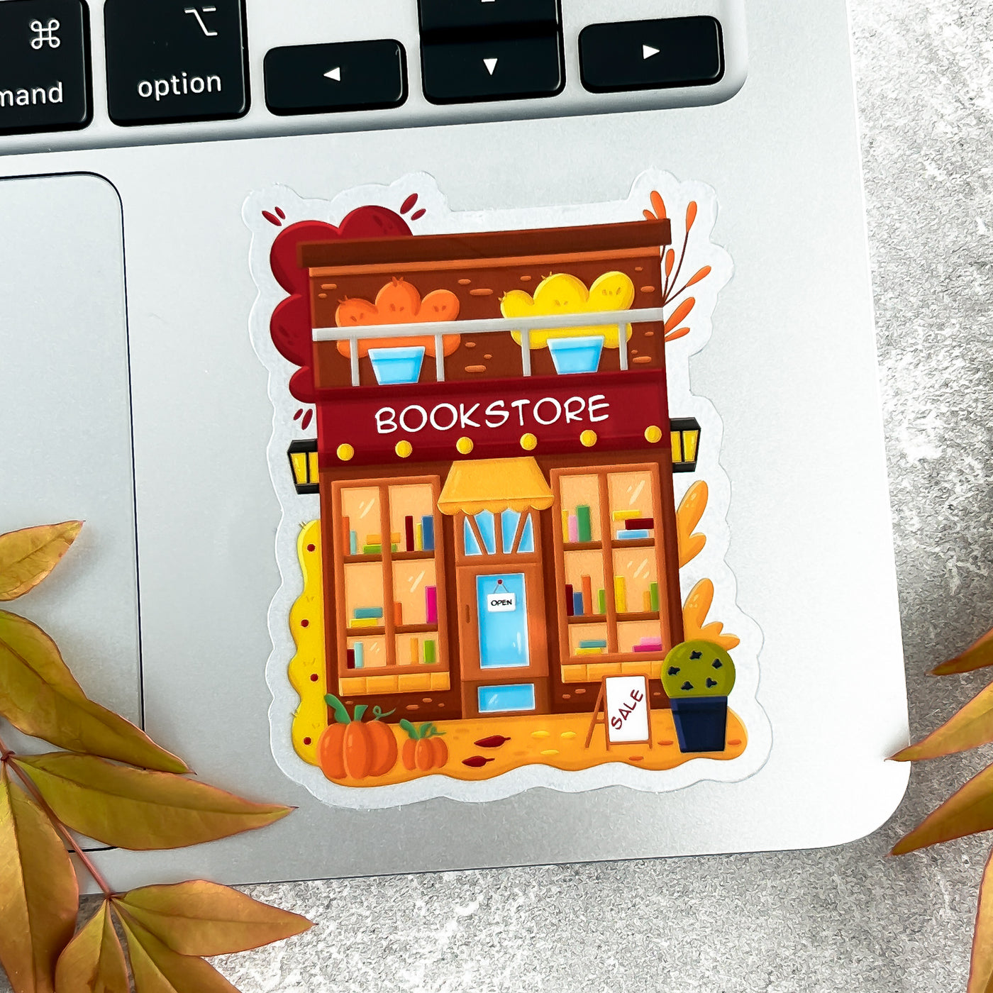 Illustrated sticker of a bookstore on a laptop keyboard with autumn leaves.
