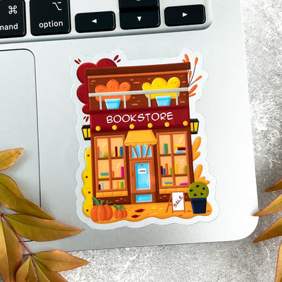 Illustrated sticker of a bookstore on a laptop keyboard with autumn leaves.