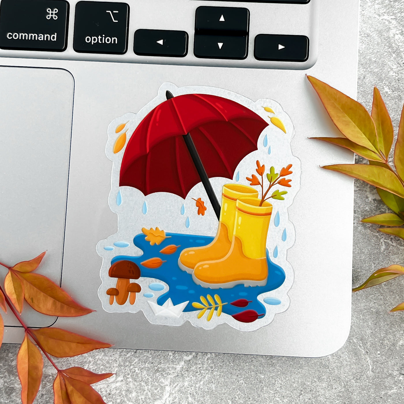 Sticker of yellow rain boots and a red umbrella on a laptop with autumn leaves.