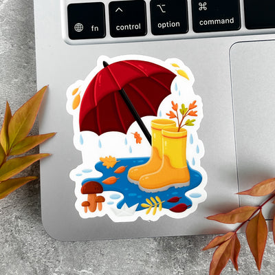 Sticker of yellow rain boots and a red umbrella on a laptop keyboard.