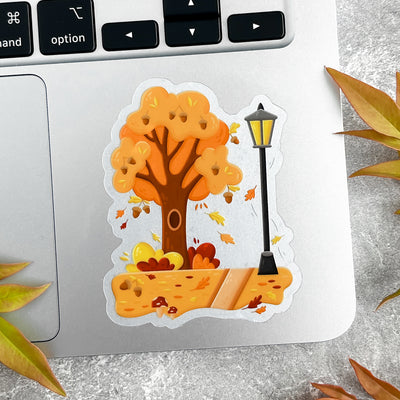 Autumn-themed sticker with tree and lamp post on a laptop.