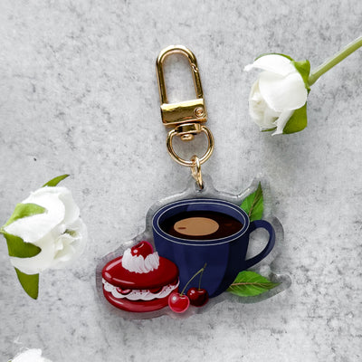 Keychain with a blue coffee cup design on a gray surface with white flowers.