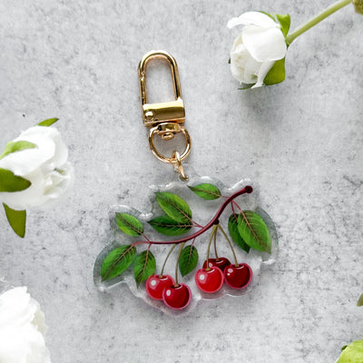 Keychain with cherry design on a gray surface with white flowers.