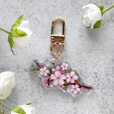 Keychain with cherry blossom design on a gray surface with white flowers.