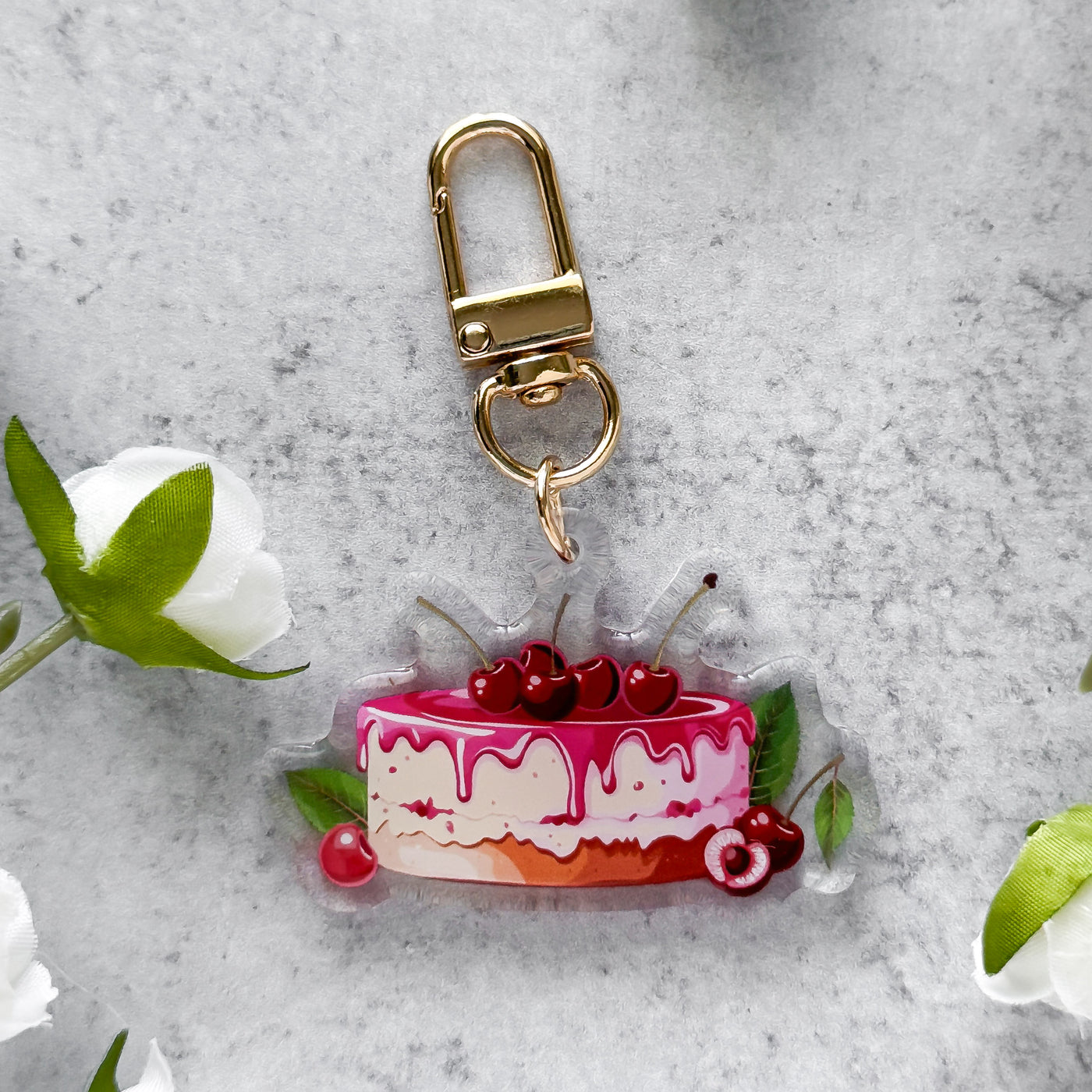 Keychain shaped like a cake with cherries on a gray surface with flowers.