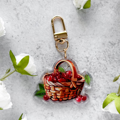 Keychain with a basket of cherries design on a light gray background with white flowers.