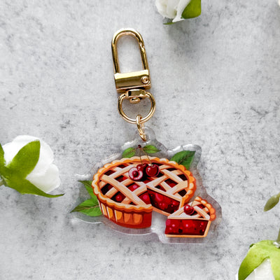 Keychain with pie design on a gray surface with flowers.