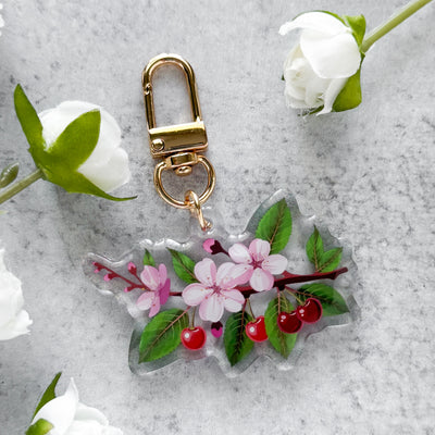 Floral keychain with cherry blossoms on a gray surface with white flowers.