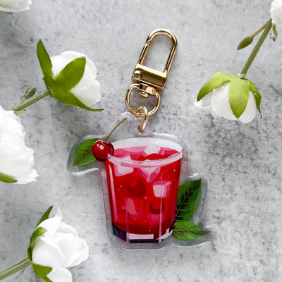 Keychain with a red drink design surrounded by white flowers on a gray surface.
