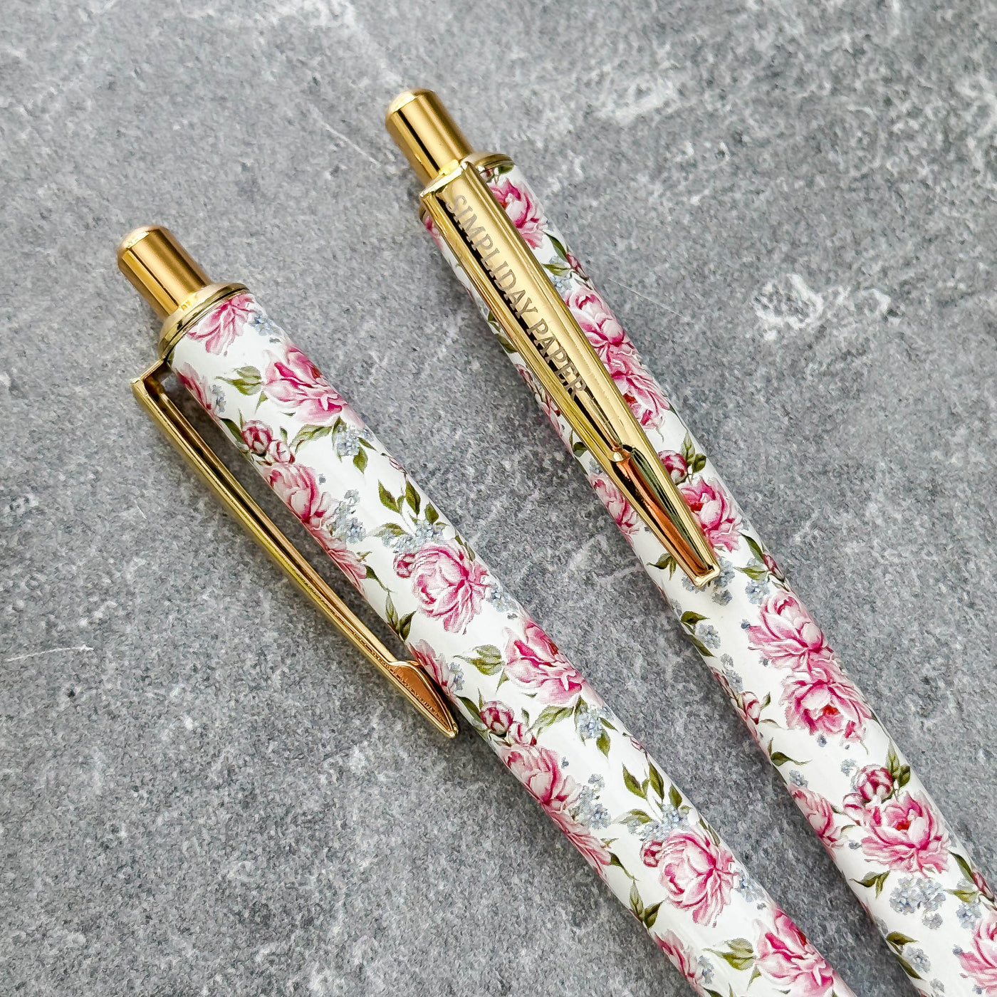 Two floral-patterned pens with gold accents on a gray surface