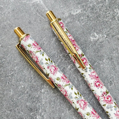 Two floral-patterned pens with gold accents on a gray surface