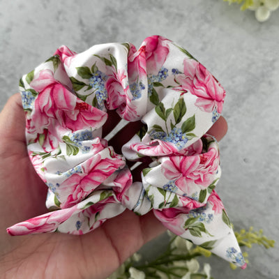 Floral patterned scrunchie held in a hand against a neutral background.