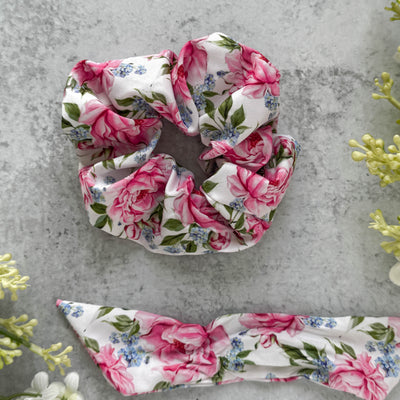 Floral scrunchie and bow on a gray surface with greenery.