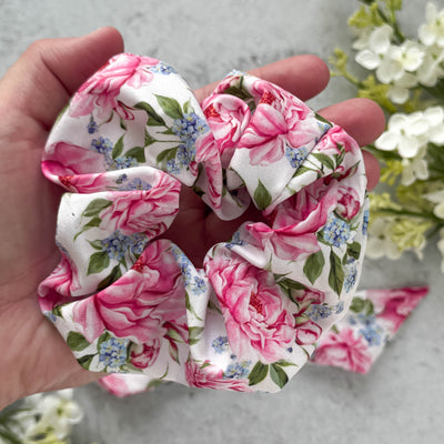 Floral scrunchie held in a hand with flowers in the background.
