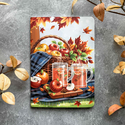 Notebook cover with autumn design featuring apples, a basket, and mugs on a gray background.