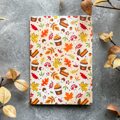 Notebook with autumn-themed cover featuring leaves, pumpkins, and other fall elements on a gray surface.