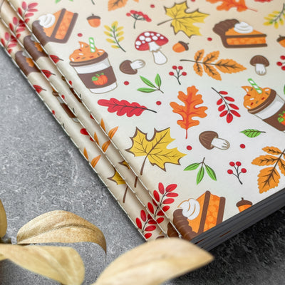 Notebook with autumn-themed cover design featuring leaves, pumpkins, and other fall elements on a gray surface.