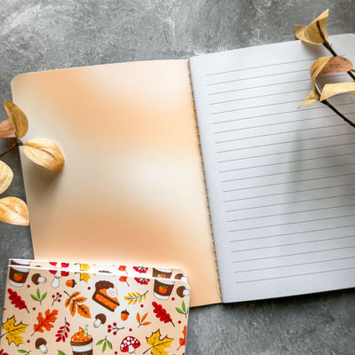 Open notebook with lined pages and a small pouch with autumn-themed design on a gray surface.