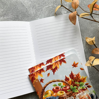 Notebook with a decorative autumn-themed card on a gray surface with leaves.