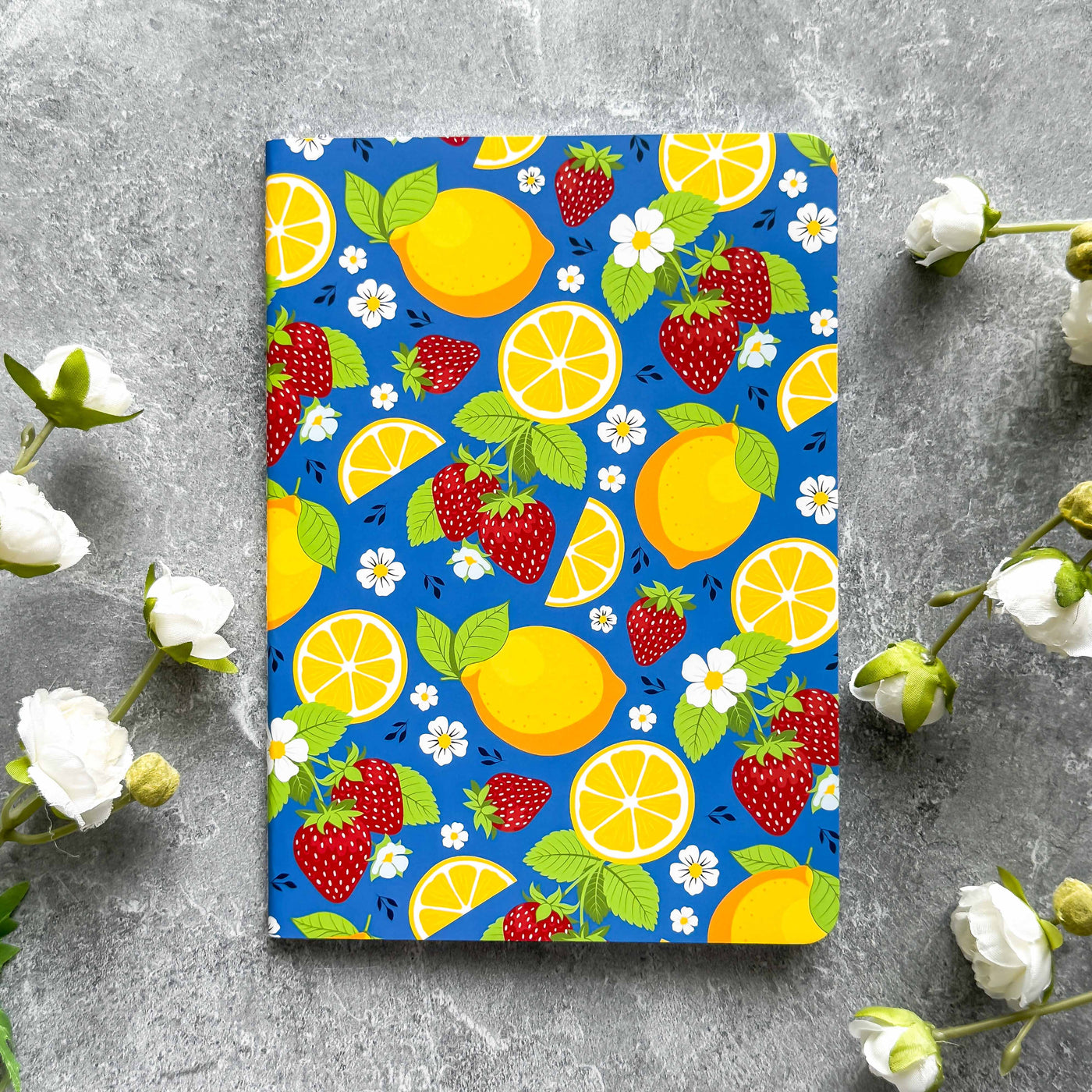 Notebook with a colorful fruit pattern on a gray surface with flowers.