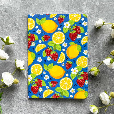 Notebook with a colorful fruit pattern on a gray surface with flowers.