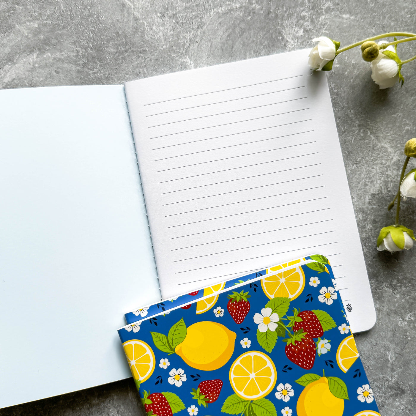 Open notebook with a colorful pouch featuring lemons and strawberries on a gray surface.