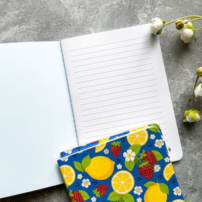 Open notebook with a colorful pouch featuring lemons and strawberries on a gray surface.