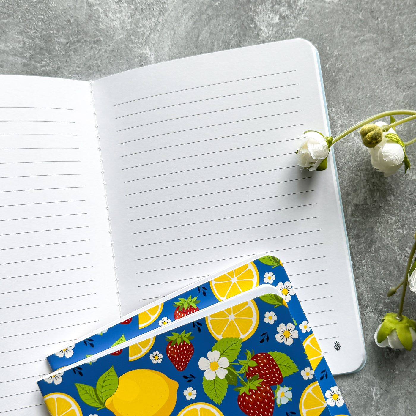 Open notebook with a colorful fruit and flower patterned cover on a gray surface.