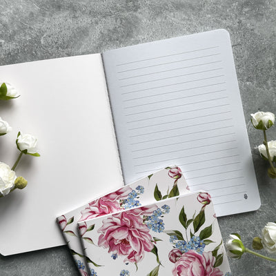 Floral notebook cover with a white notebook on a gray surface with flowers.