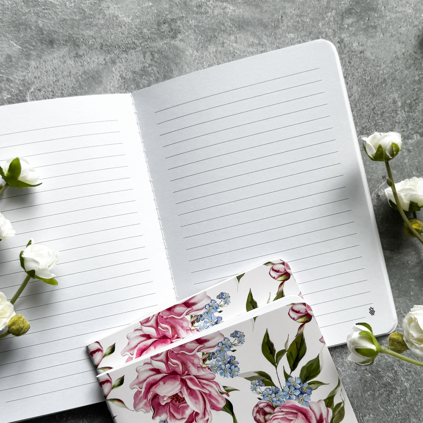 Open notebook with floral bookmark on a gray surface with flowers.