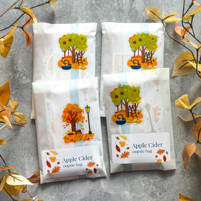 Four packages of 'Apple Cider' oopsie bags with autumn-themed designs on a gray surface.
