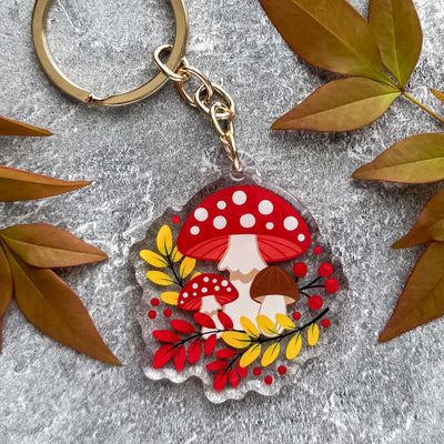 Keychain with mushroom design surrounded by autumn leaves on a textured surface.