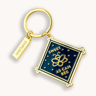 Midnight bee metal keychain is made out of hard enamel, filled and sealed. Each one is durable and waterproof. Features text on the front "SWEET AS CAN BEE". The back side of keychain features a word "STRENGTH &amp; WISDOM" on solid gold background, that can work as a tiny mirror.